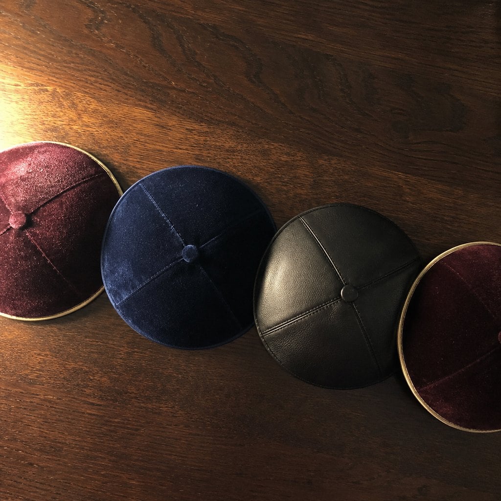 Custom velvet and leather kippahs with gold rims on a walnut table